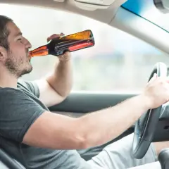 Mężczyzna pije piwo za kierownicą. To niebezpieczna jazda po alkoholu, która może skończyć się tragicznie.