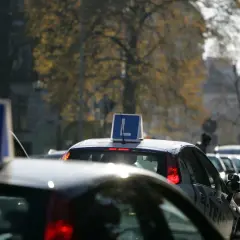 Samochody nauki jazdy z literą "L" na dachu stoją w korku ulicznym.