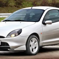 Srebrne coupe Ford Puma z polskimi tablicami rejestracyjnymi PCT 20558 stoi na brukowanej nawierzchni.