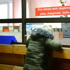 Osoba w zielonej kurtce przy okienku urzędu, znak "Uwaga obiekt monitorowany".