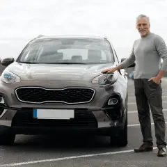 Starszy mężczyzna stoi obok brązowego SUV-a na parkingu.