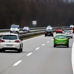 Samochody poruszają się po autostradzie, każdy na swoim pasie ruchu. Zielony samochód z przodu wyznacza tempo.