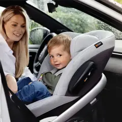 Kobieta w białej koszuli patrzy na dziecko w foteliku samochodowym na przednim siedzeniu.