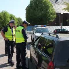 Policjanci wypisują mandat za jazdę po chodniku. Jeden z funkcjonariuszy spisuje dane kierowcy w samochodzie.