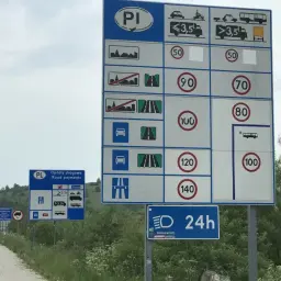Znaki drogowe informujące o opłatach i limitach prędkości na drogach w Polsce. Widoczne są różne ograniczenia prędkości dla samochodów i pojazdów ciężarowych.