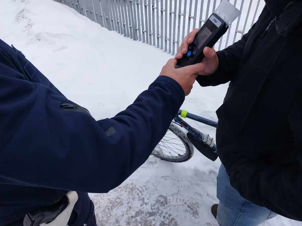 Policjant bada alkomatem rowerzystę. Niebezpieczna jazda rowerem po alkoholu może skończyć się mandatem.