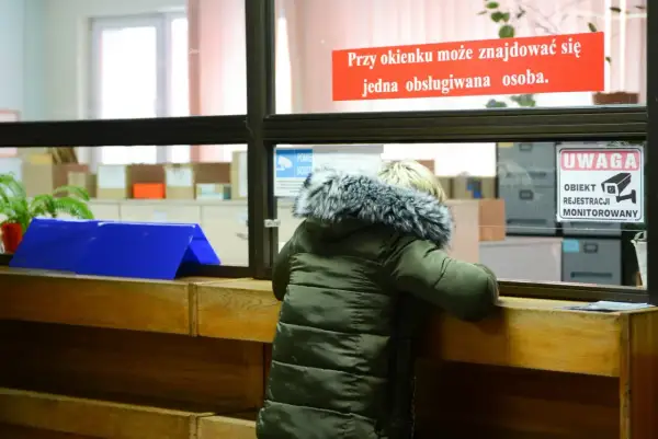 Osoba w zielonej kurtce przy okienku urzędu, znak "Uwaga obiekt monitorowany".