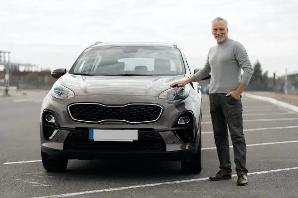 Starszy mężczyzna stoi obok brązowego SUV-a na parkingu.