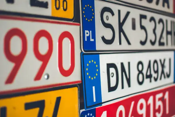 Zbliżenie na stos tablic rejestracyjnych z kodami krajów UE, w tym PL, SK i DN.
