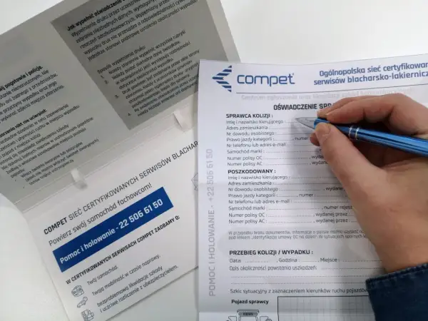 Dłoń z długopisem wypełniająca formularz oświadczenia sprawcy kolizji drogowej.