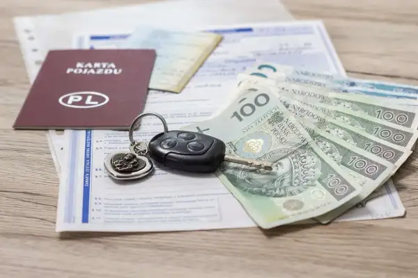 Karta pojazdu, kluczyki samochodowe i polskie banknoty 100 zł leżą na dokumentach.